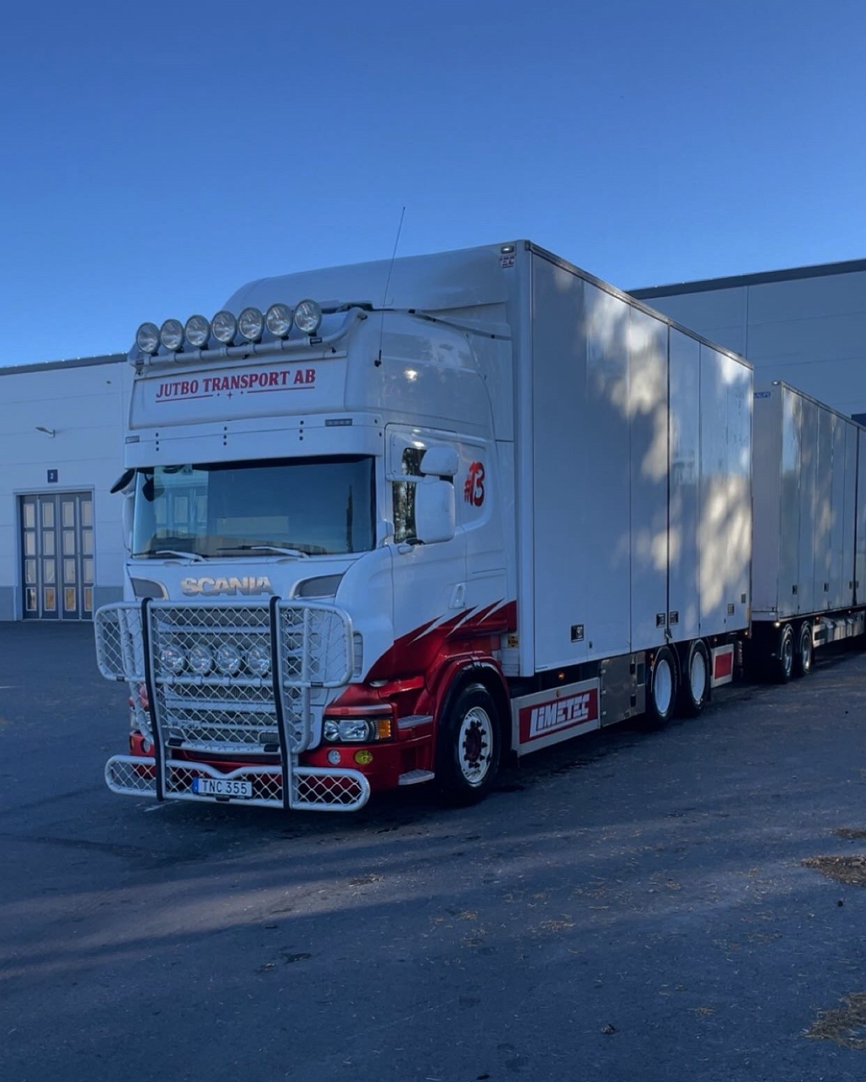Scania med släp från Jutbo Transport parkerad framför en lagerbyggnad