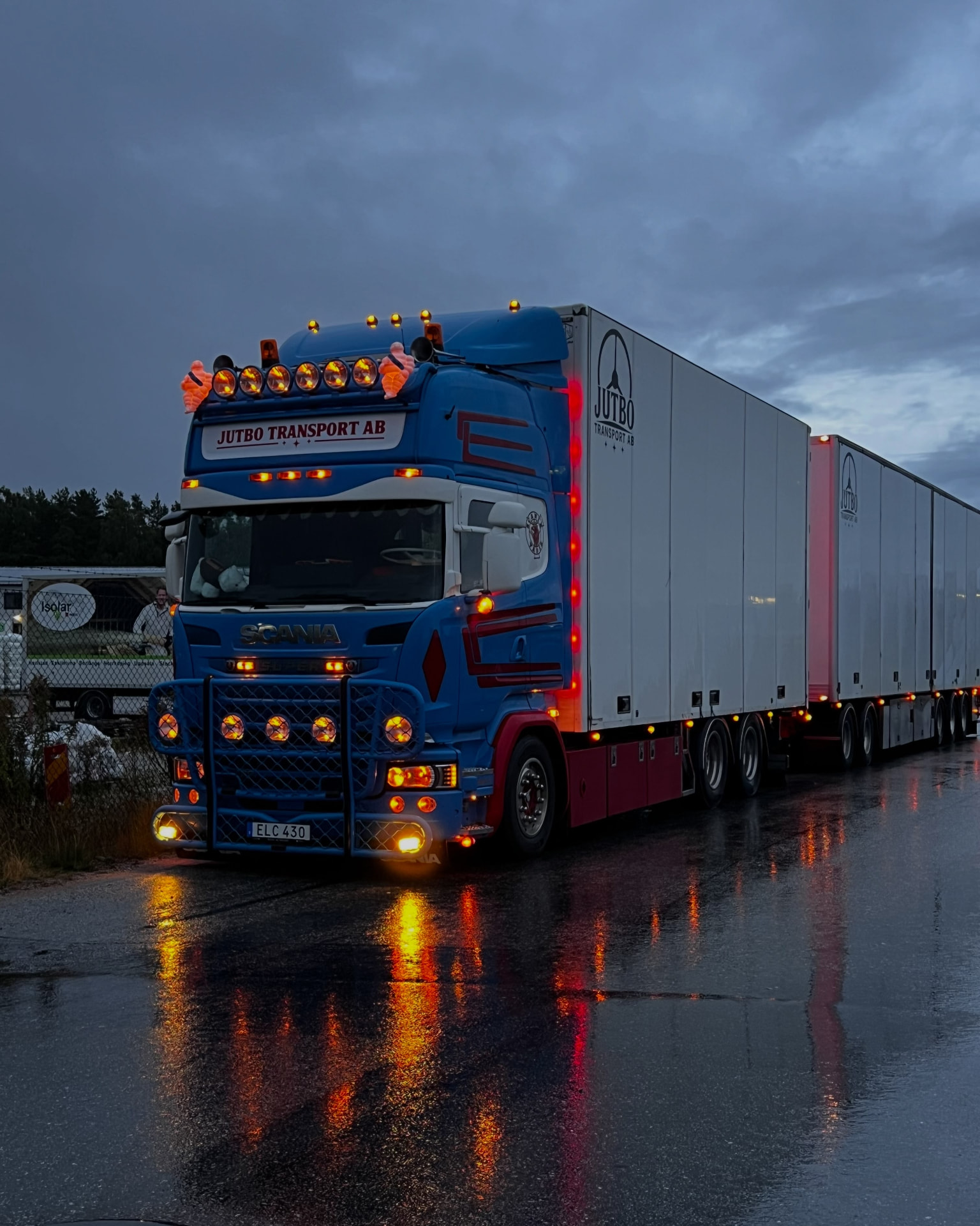 Blå Scania från Jutbo Transport på blöt asfalt i skymningen