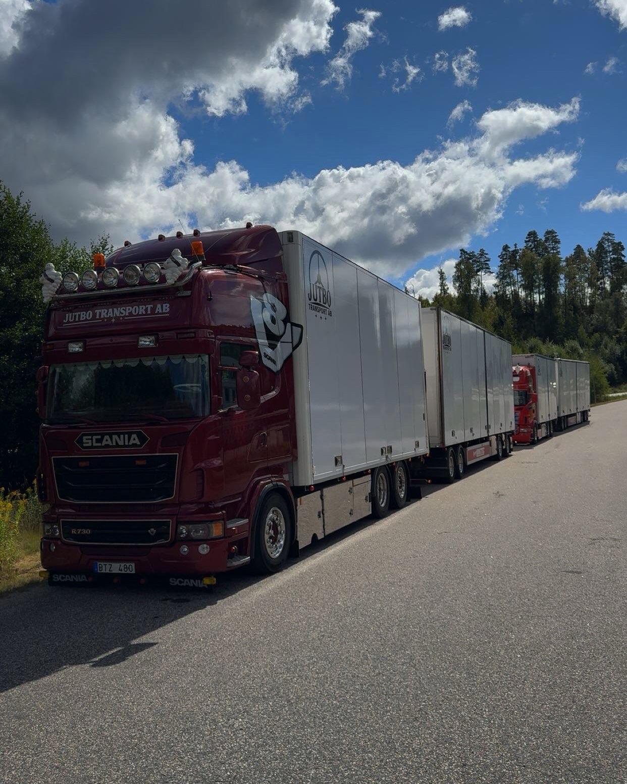 Mörkröd Scania med flera släp från Jutbo Transport längs en väg